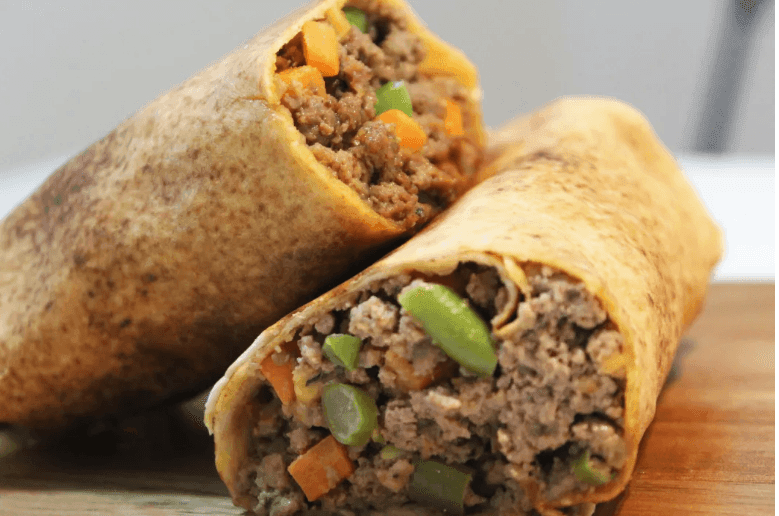 Close-up of two beef burritos with visible green and orange peppers on a wooden surface.