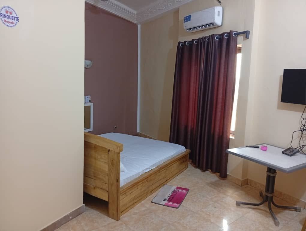 Small bedroom with wooden bed, wall-mounted TV, air conditioner, and burgundy curtains.