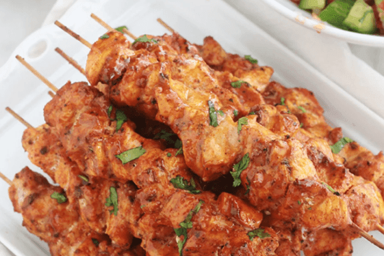 Plate of grilled chicken skewers garnished with herbs.