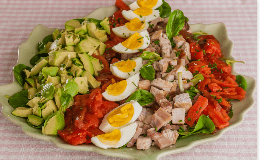 Plate of Cobb salad with avocado, tomatoes, eggs, and diced chicken on a green dish.