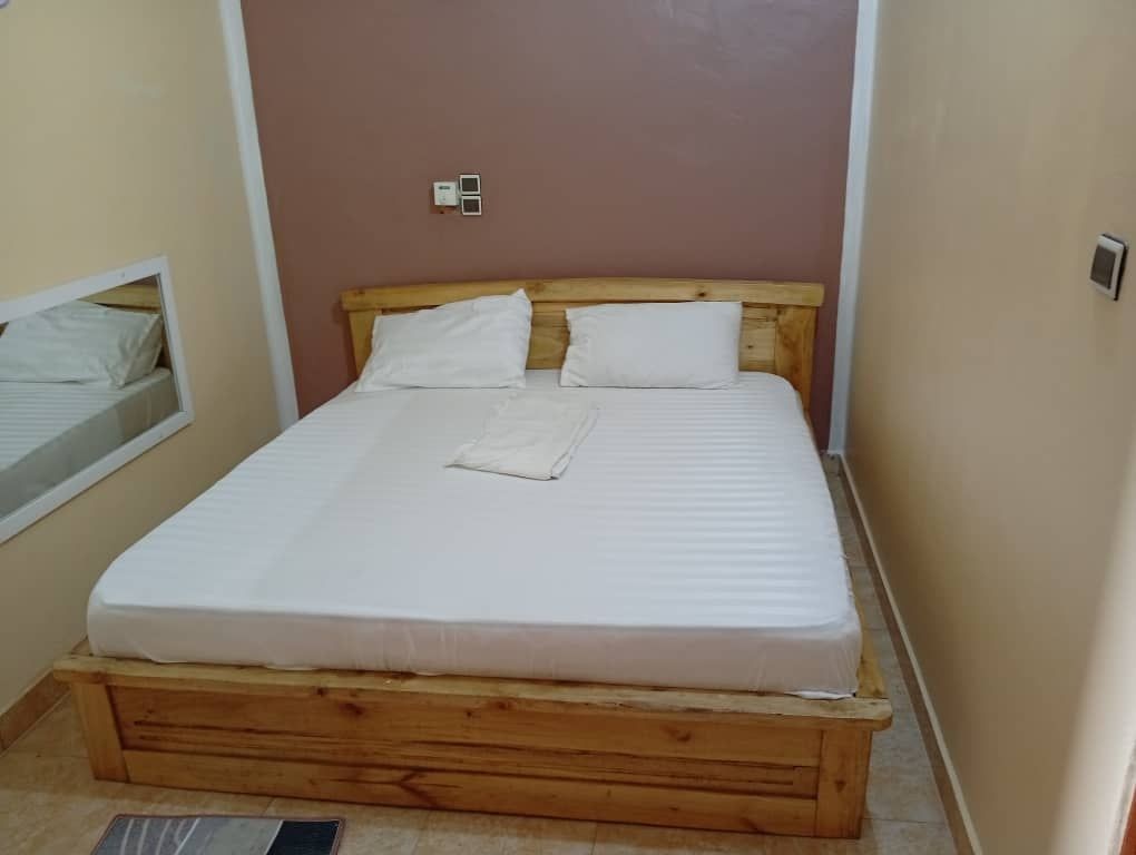 Simple bedroom with a wooden bedframe and white bedding against beige walls.