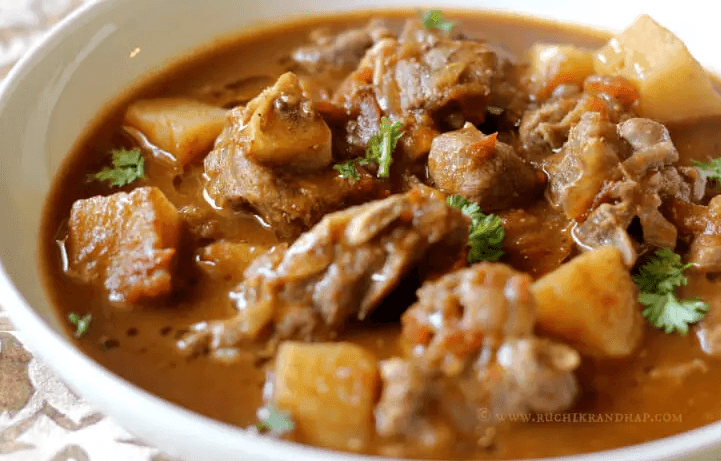 Close-up of a bowl of spicy curry with meat pieces and potatoes garnished with cilantro.