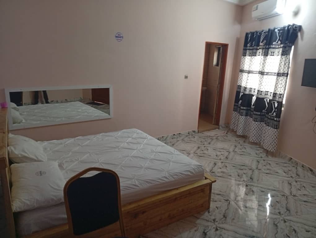 Simple bedroom with a bed, mirror, curtains, and tiled floor.