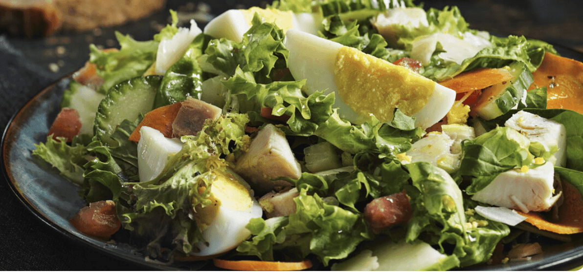 Plate of salad with lettuce, cucumber, boiled egg, carrots, and chicken pieces.