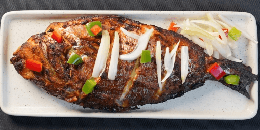 Grilled fish on a plate garnished with sliced onions and bell peppers.