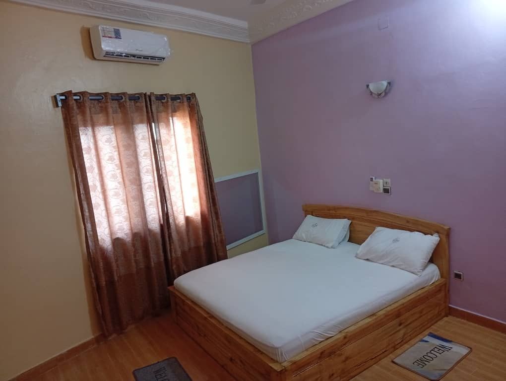 Clean bedroom with a large wooden bed, brown curtains, air conditioning unit, and purple walls.