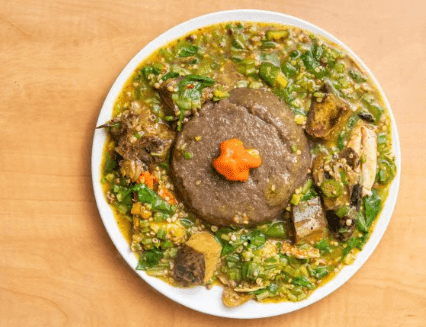 Plate of African soup and fufu with assorted vegetables and meat.