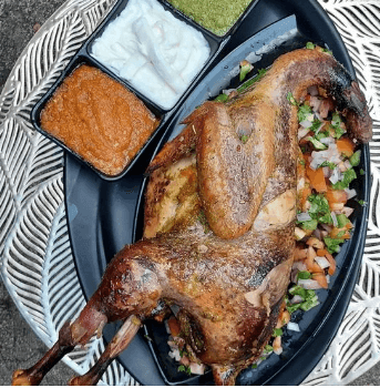 Roasted duck on a platter with three sauces and chopped vegetables as garnish.